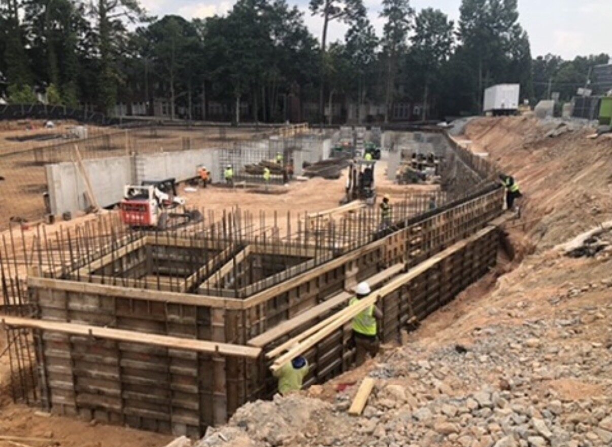 Foundation excavation with skid steer, formwork, and crews staged in sequence