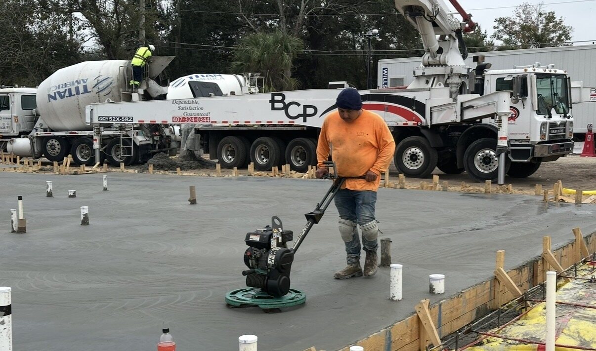 Crew member finishing slab edges with pump truck and mixer fleet staged behind