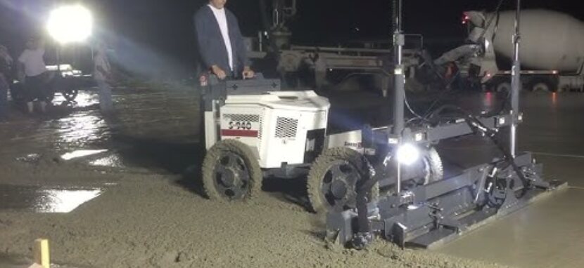 Walk-behind laser screed leveling a slab during a night pour