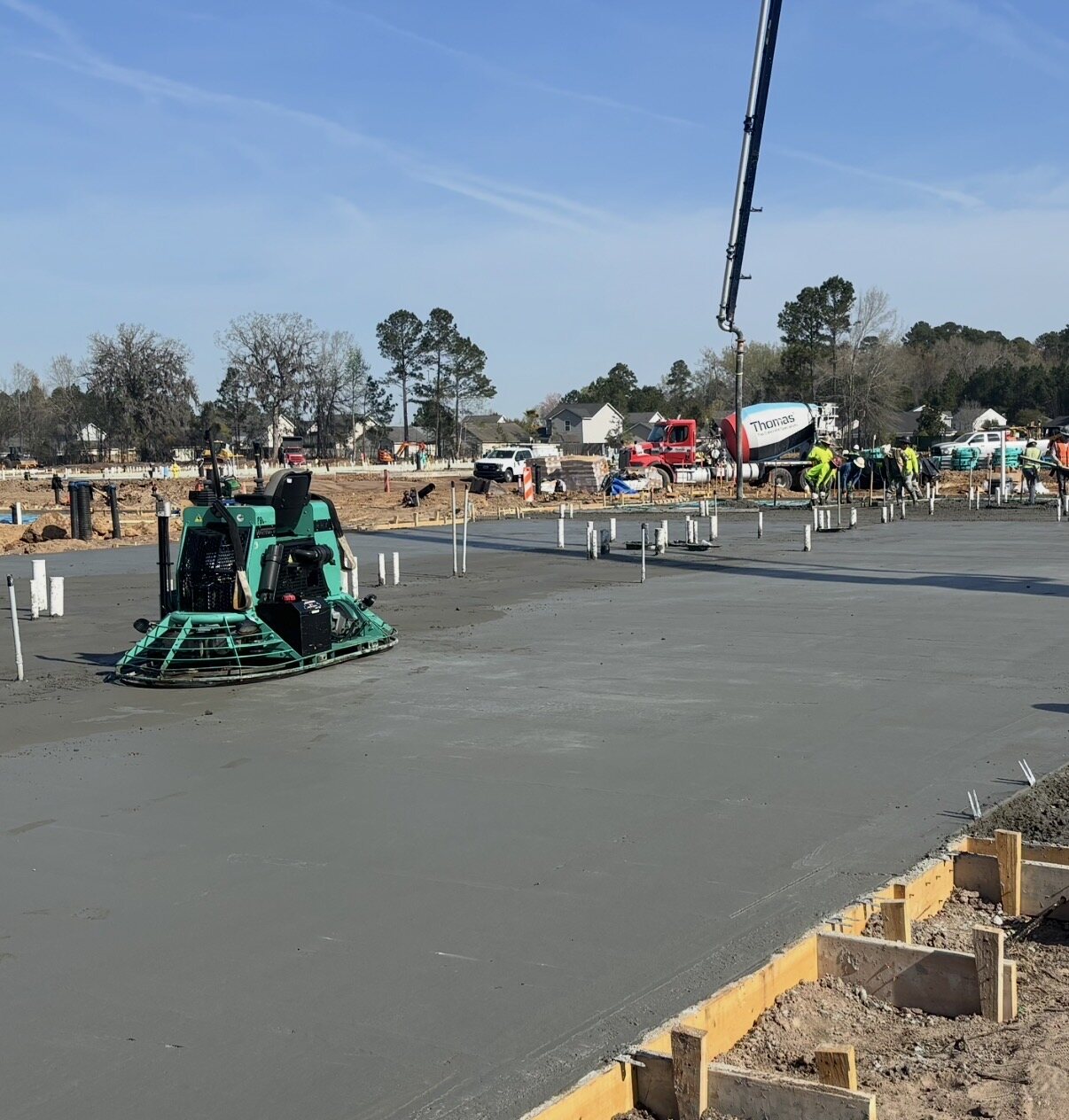 Ride-on trowel finishing a large slab with pump boom overhead